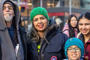 Shaheen Moledina, Candidate for Town of Aurora Councillor, Ward 4, stands with her family at a community gathering. Shaheen, wearing a bright green knit hat and a navy blue winter parka, is surrounded by her children—her son in the teal hat and her daughter—along with an older family member. This image highlights her active presence in the Aurora community and her personal dedication to the families of Ward 5, where she has lived and raised her own children since 2010.
